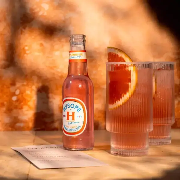 Cette image représente une bouteille de soda pamplemousse à côté d'un verre rempli et décoré d'une tranche de pamplemousse.