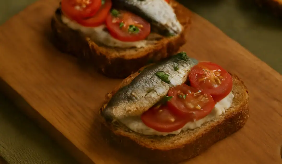 Tartine à la sardine sur pain grillé avec tomates cerises et herbes fraîches, posée sur une planche en bois – visuel d’illustration pour un article de recettes simples.