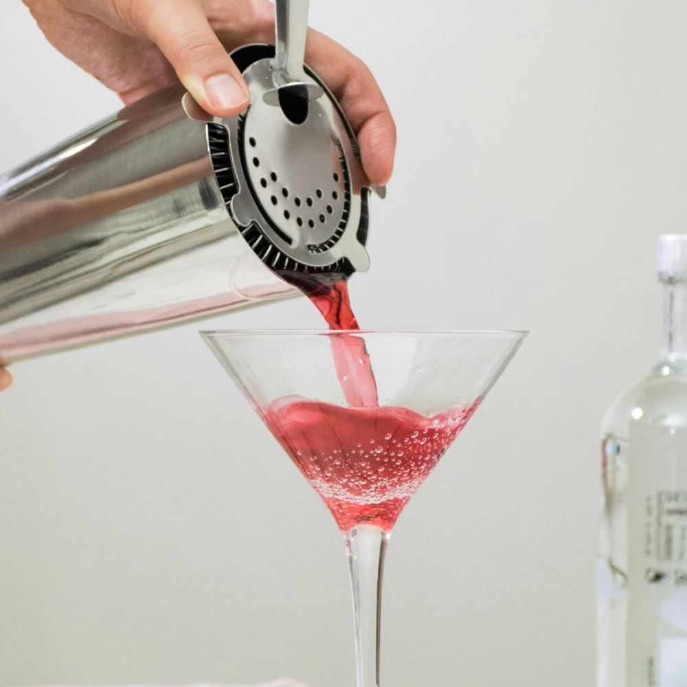Vue rapprochée d'un cocktail rouge versé depuis un shaker en inox dans un verre à martini, atelier cocktail près d'Annecy.